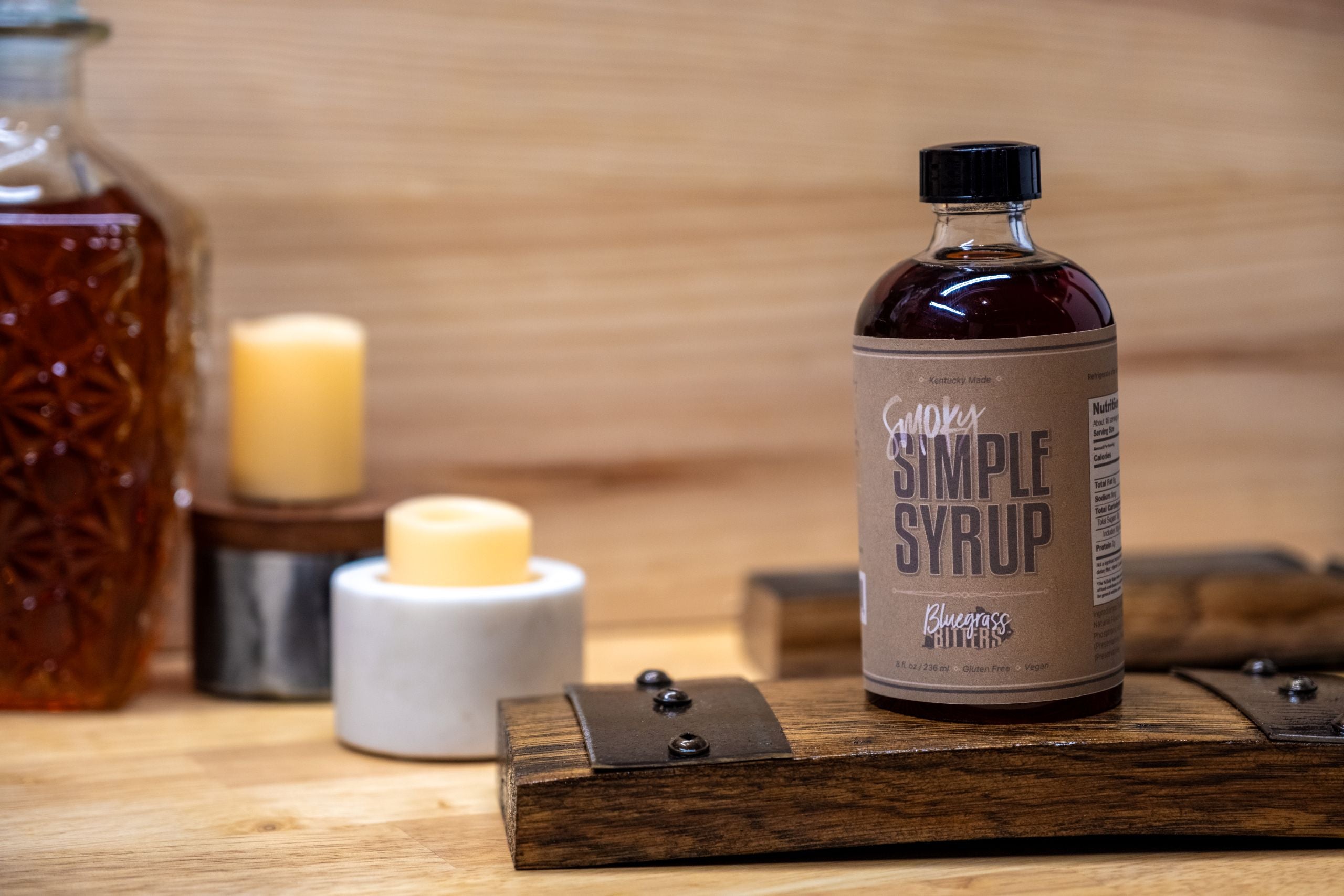 Bottle of Smoky Simple Syrup on a wooden stave with candles and another bottle in the background.