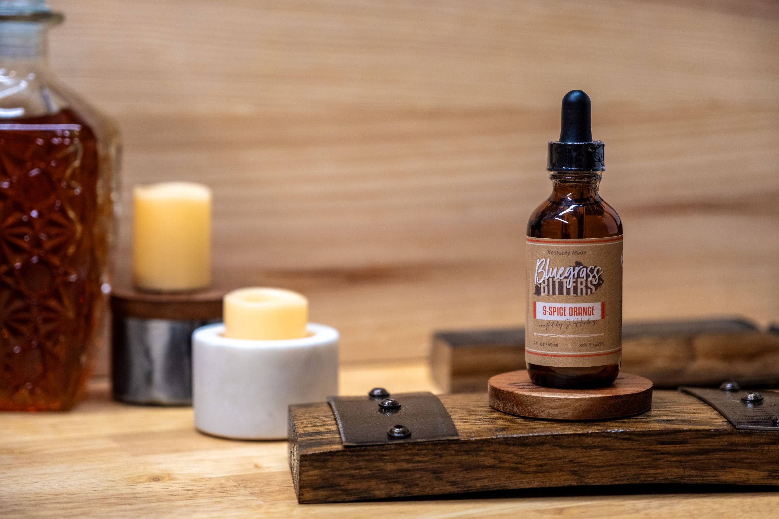 Bottle of Bluegrass Bitters on a wooden surface with candles and another bottle in the background.