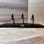 Three Bluegrass Bitters dropper bottles on a wooden stave stand against a wooden background
